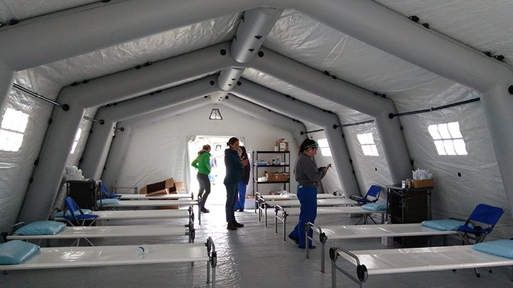 The inside of a tent with beds setup and a few nursing professionals ready to serve patients.