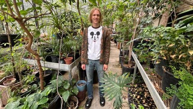 A student stands in a greenhouse smiling.