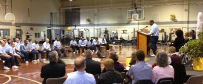 Student inmates gather seated to listen to a speaker from a pulpit.