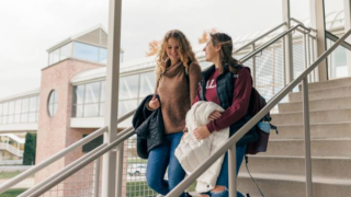 Two girls smile while walking down an outdoor stairway on the Calvin University campus.