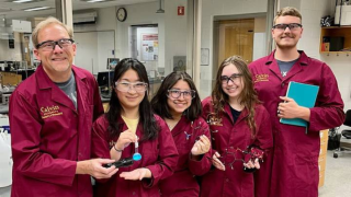 A professor and four students all in maroon lab coats smile at the camera.