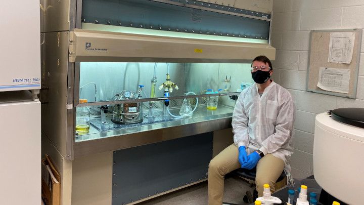 A research assistant sits next to his experiment that he's conducting within a laboratory.