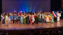 A large group of students holding flags stands on stage after a performance.
