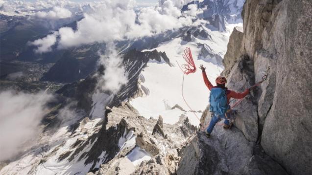 A climber looks down on an expanse, below a mountain.