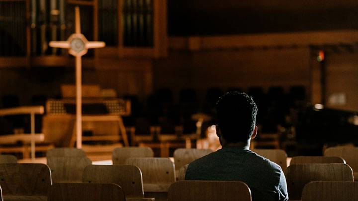 A student prayers in a darkened Chapel before the cross.