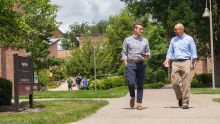 A student and a professor talk with each other as they walk on a campus path.