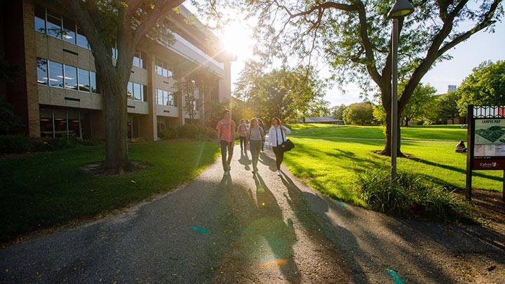 Three students walk east down a campus pathway with the sun at their backs.