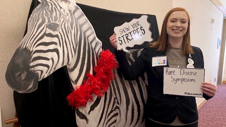A female college student in a suit coat stands next to a Zebra cutout.