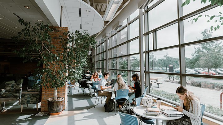 Students study at a few circular tables in an open space with lots of natural light.
