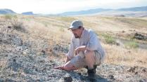 A professor kneals to study the rocky plains beneath his feet.