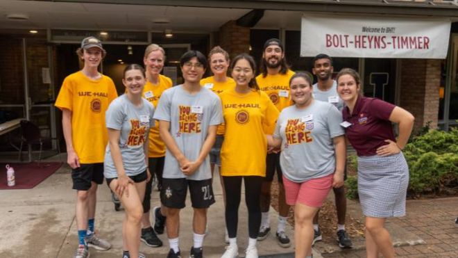 Students in yellow and gray shirts posing during Move-In Day in front of a residence hall.