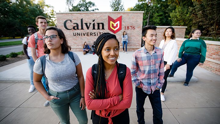 Students posing in front of the Calvin University entrance sign.