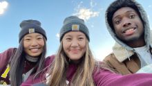 Three students take a selfie with a blue sky behind them.