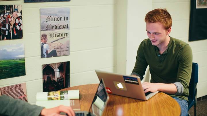 Student at table using laptop, smiling
