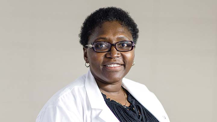 A woman in glasses and a lab coat smiles and looks straight ahead.