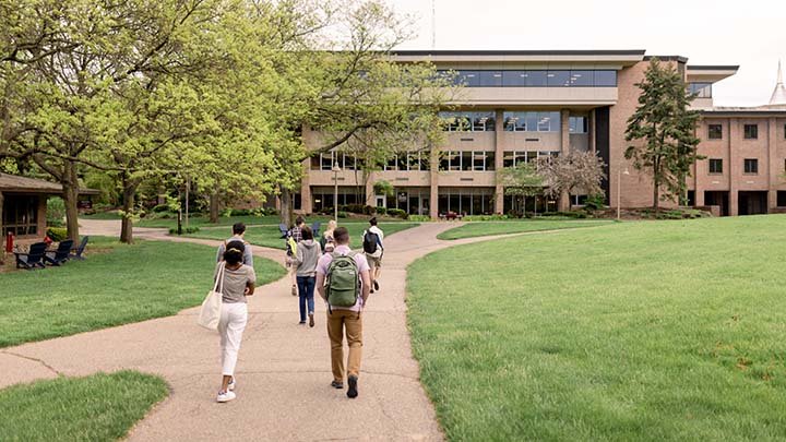 Students walking on a path past a green lawn toward an academic building
