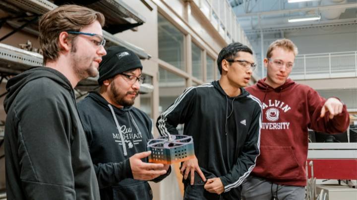 Four students look off screen, one holds a robot that's about to go into combat at Calvin University