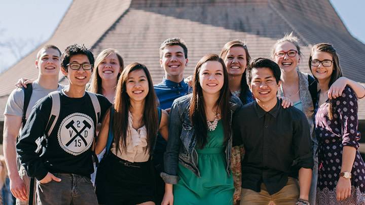 A group of students smiles for the camera in front of the Calvin Chapel