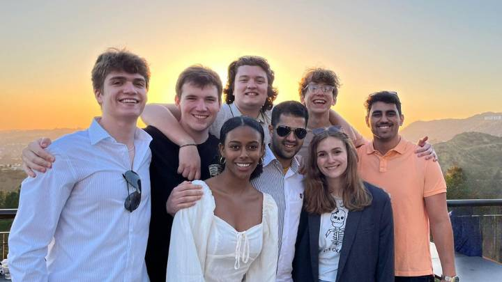 A group of eight students posing together at sunset with Hollywood sign and mountains in backdrop.
