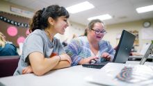 Two students smiling as they work on a computer