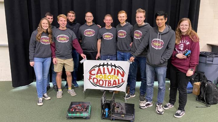Nine students and their faculty adviser pose with robots and hold a 