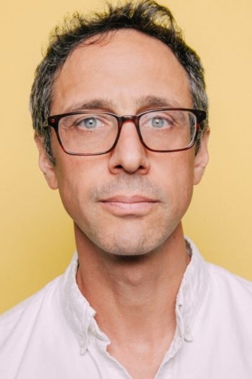 Jacob, a white man with grey hair and glasses, wears a white-collar shirt in a professional headshot in front of a yellow background.