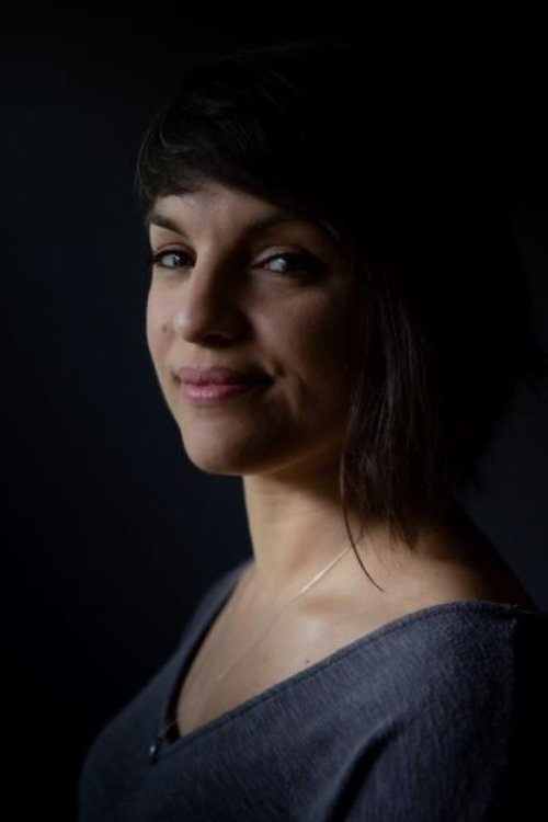 Monica, a Latina woman with dark hair, poses for a headshot against a dramatic black background.