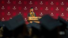 From the perspective of a graduate: A student in cap and gown at podium on stage.