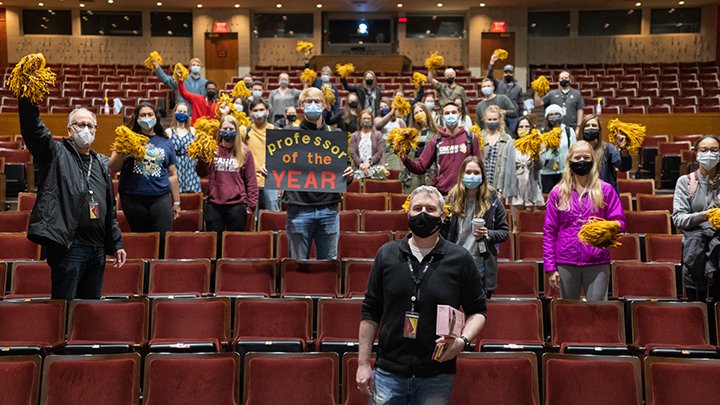 Students and professors in masks stand behind Professor John Wertz with signs of congratulations!
