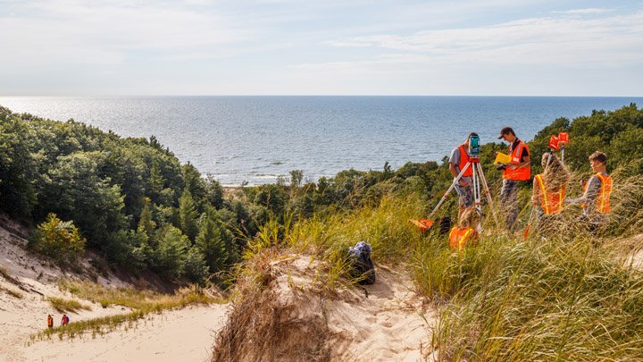 Students standing at the top of a dune along Lake Michigan using research equipment.