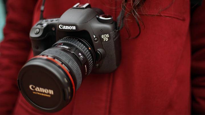 A Canon 7D camera hangs around the neck of photographer wearing a maroon fleece jacket.