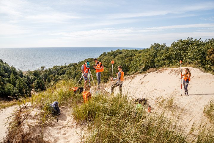 College-age students stand on top of a dune overlooking Lake Michigan doing research.