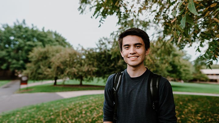 Photo of Calvin student Manato Jansen with his bookbag on and an open greenspace behind him.