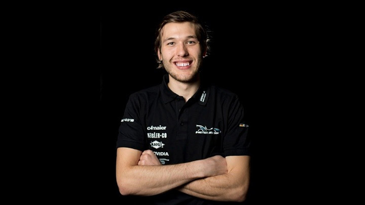In front of a black background, a male student smiles and crosses his arms.