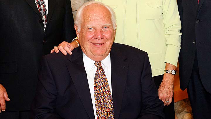 A headshot of Doug Nagel seated and smiling in a dark suit, white shirt, and colorful tie.