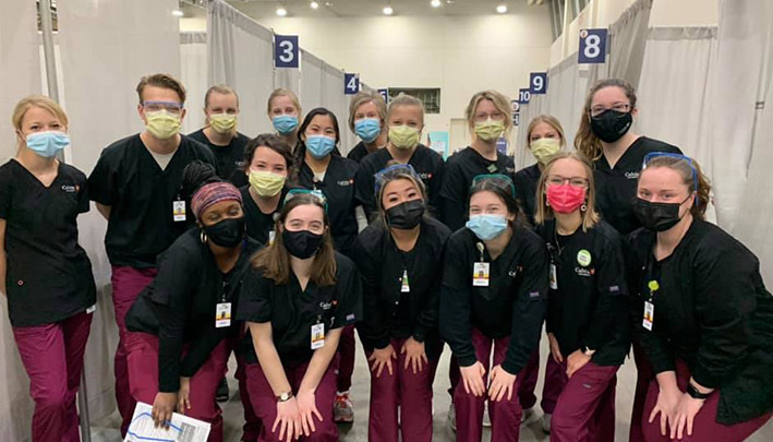 About a dozen nurses in scrubs and masks pose for a photo at an indoor COVID-19 vaccination clinic.