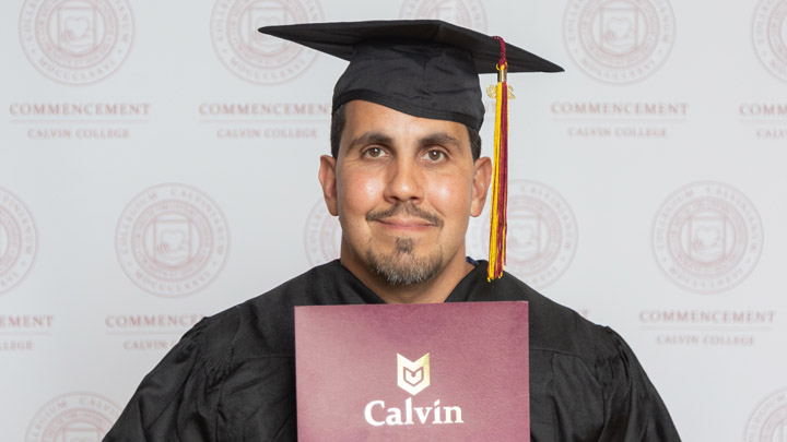 A photo of an adult male holding a diploma with cap and gown on