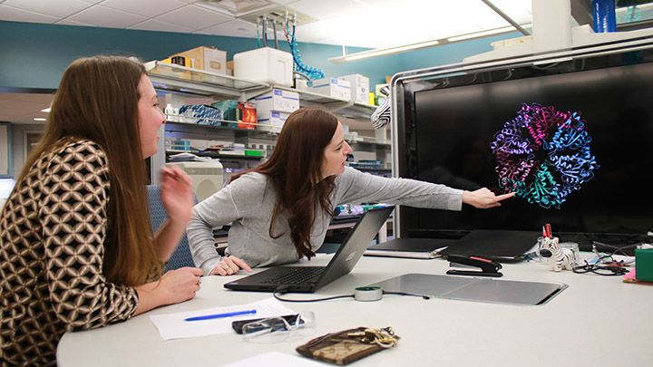 Professor Rachael Baker watches professor Amy Wilstermann point at a diagram on a screen.