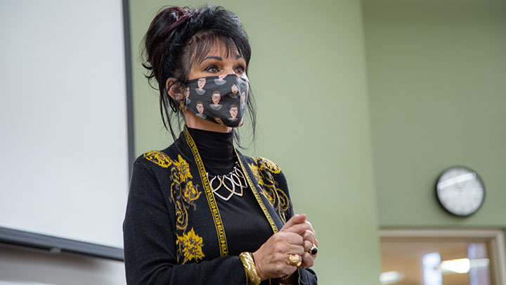 A woman stands in front of a whiteboard in a mask speaking to a classroom of students.