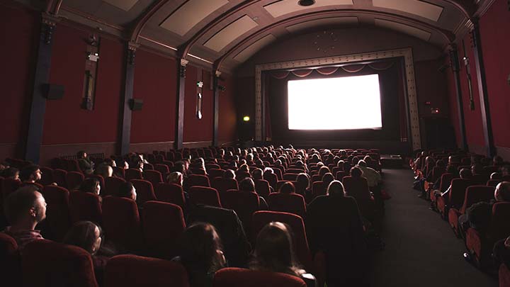 A movie theater full of people with a big screen up front and red walls on each side