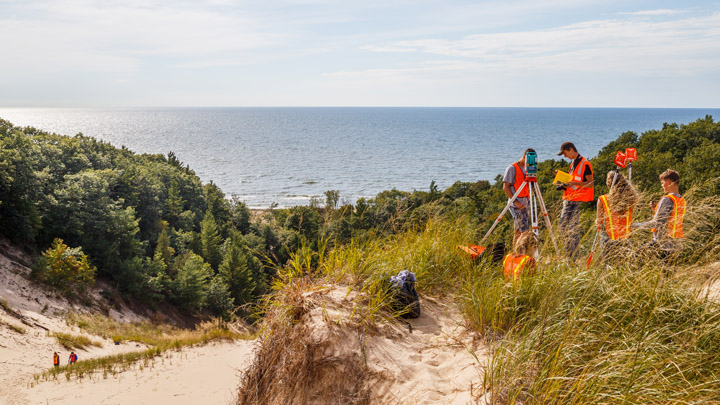 Students standing at the top of a dune along Lake Michigan using research equipment.