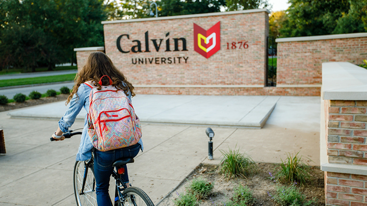 A student rides her bike near the Calvin University entrance sign.
