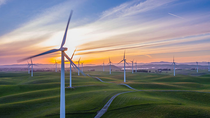 A wind farm set on some rolling hills at sunset