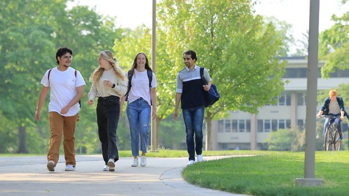 4 students walk and talk on the Calvin University campus in Spring 2023. A bicyclist in background.