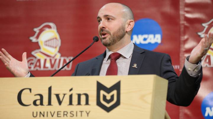 Head Football Coach Trent Figg speaking behind Calvin Univerity podium in suit and tie.