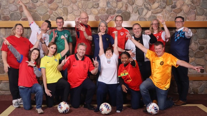 15 administrators and coaches dressed in World Cup soccer jerseys smile and pose.