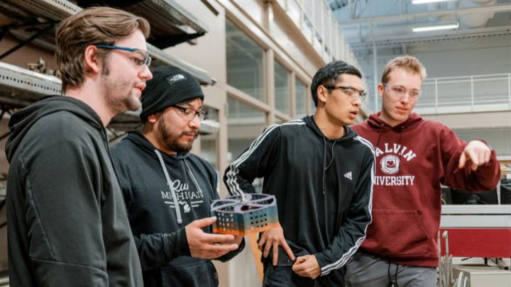 Four students look off screen, one holds a robot that's about to go into combat at Calvin University