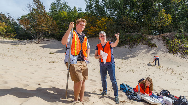 A professor and student wearing orange vests talking on a sand dune while doing field research.