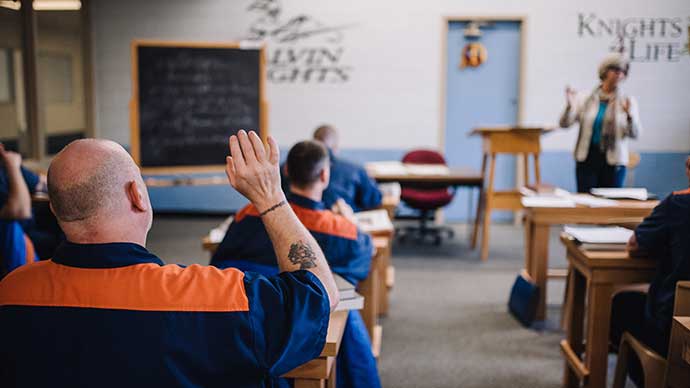 A Calvin Prison Initiative student in class, raising his hand from his desk.