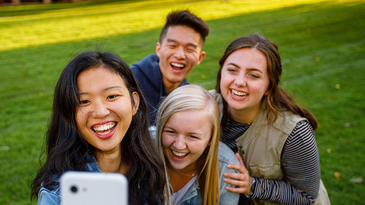 Four students huddle for a group selfie on the Commons Lawn.